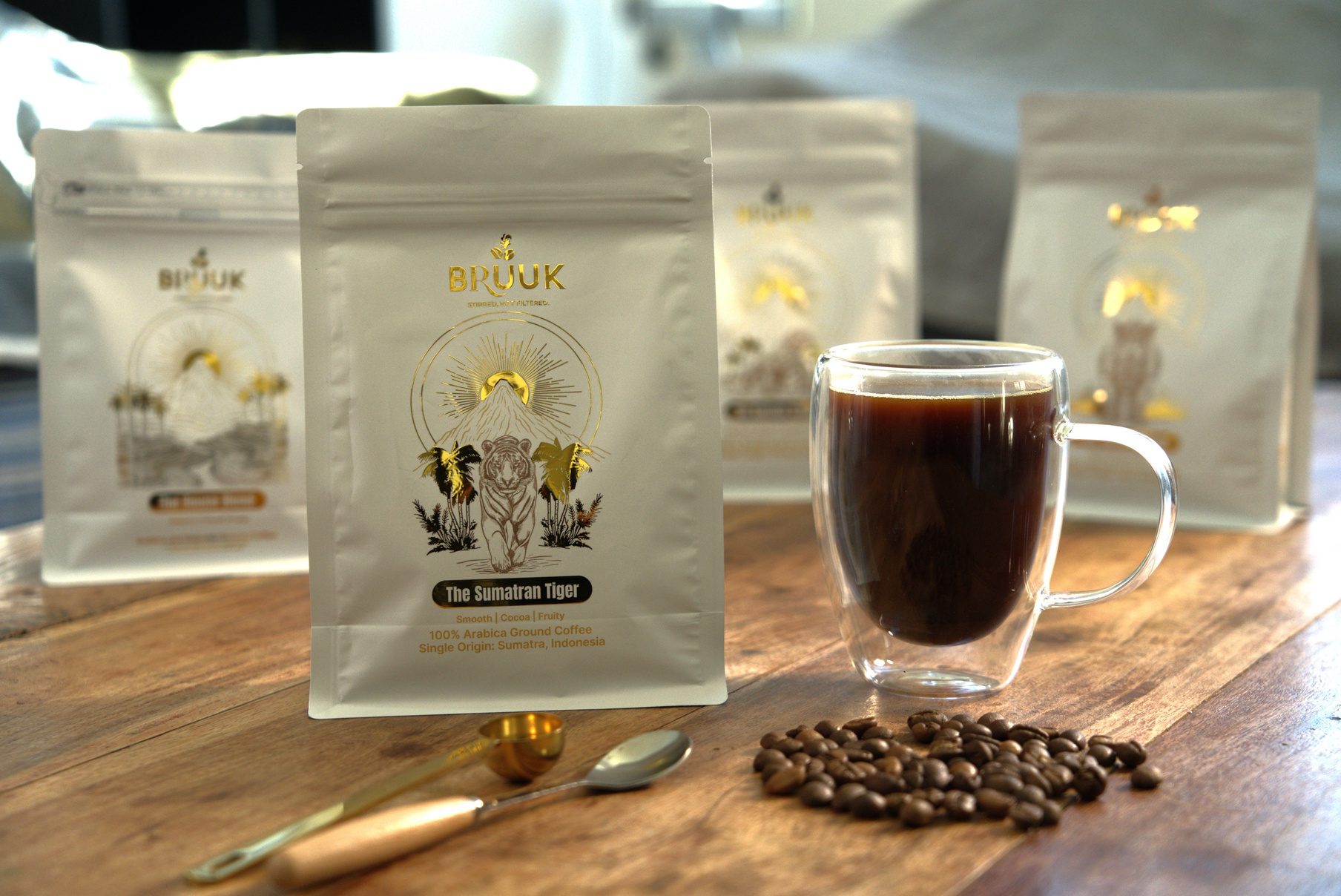 A glass of black coffee beside BRUUK coffee bags and loose beans