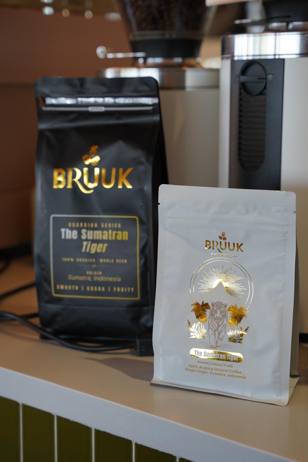 Two bags of BRUUK Sumatran Tiger, whole bean and ground, on a café counter in front of espresso grinders