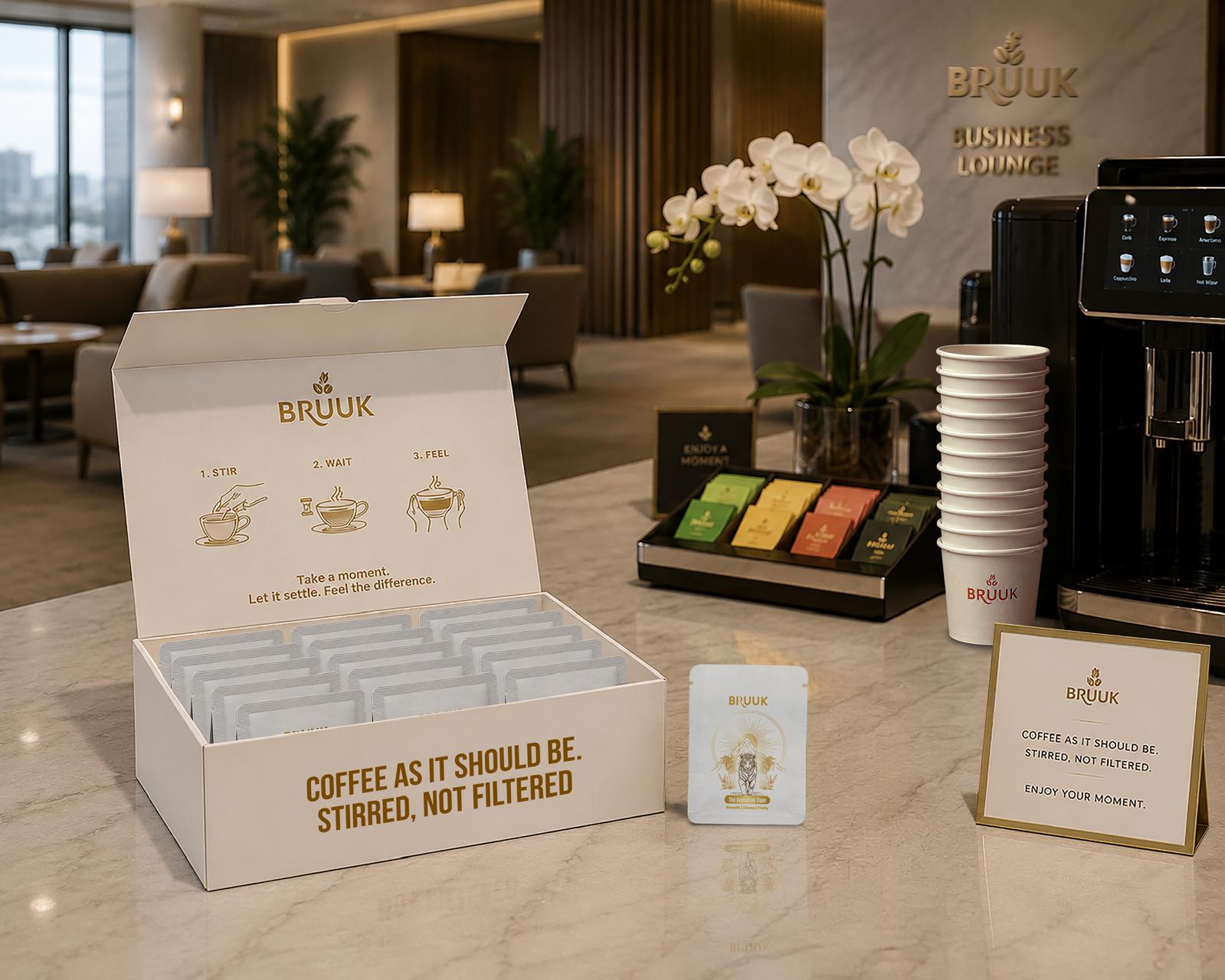 An open BRUUK box of single-serve sachets on a marble counter in a hotel business lounge, beside a Sumatran Tiger sachet and a table card